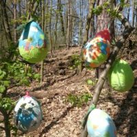 Aus Zeitungsschnipseln, die um Luftballons geklebt wurden, gebastelte Ostereier, bunt bemalt, hängen an Zweigen im Wald.