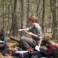 Zwei Kinder sitzen im Wald und Schnitzen.